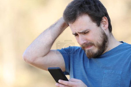 Foto de Hombre triste comprobando el mal contenido del teléfono inteligente de pie al aire libre - Imagen libre de derechos