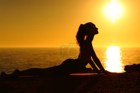 Foto de Silueta de retrato de vista lateral de un yogui al atardecer haciendo yoga en la playa - Imagen libre de derechos