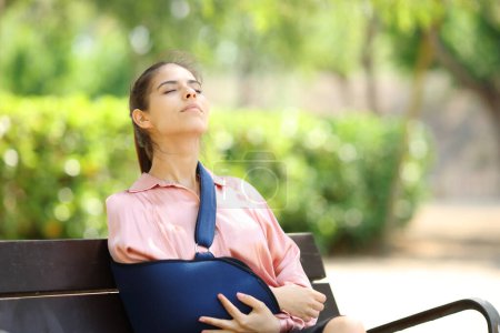 Rekonvaleszente Frau atmet frische Luft und sitzt in einem Park auf einer Bank