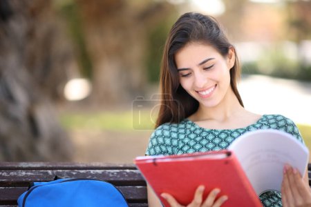 Estudiante feliz sentado en un parque estudiando solo