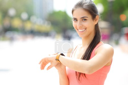 Photo for Happy runner checking smartwatch looking at you in the street - Royalty Free Image