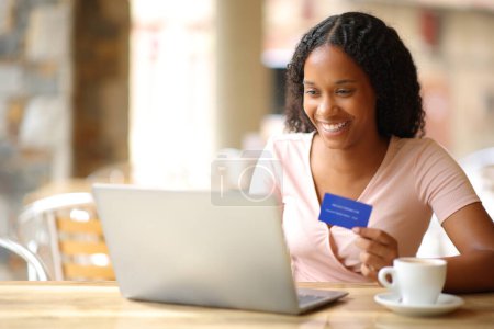 Schwarzer Online-Käufer bezahlt online mit Laptop und Kreditkarte auf Restaurantterrasse