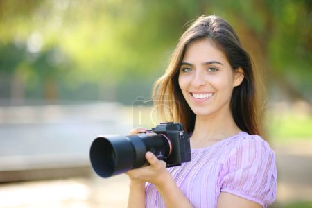 Happy photographer posing looking at camera and holding mirrorless in a park