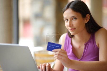 Online buyer holding credit card looking at you in a bar terrace
