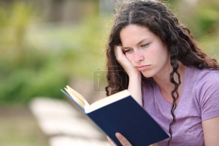 Mujer aburrida leyendo un libro de papel sentado en un parque