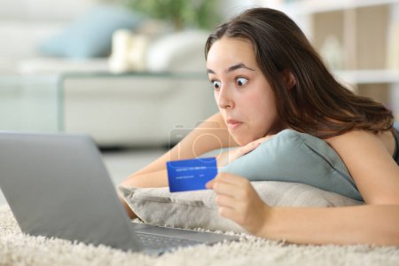 Acheteur en ligne perplexe payer avec un ordinateur portable et carte de crédit sur le sol à la maison