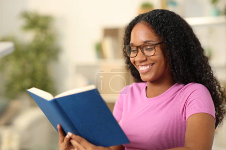 Heureux lecteur noir avec des lunettes de lecture d'un livre de papier à la maison