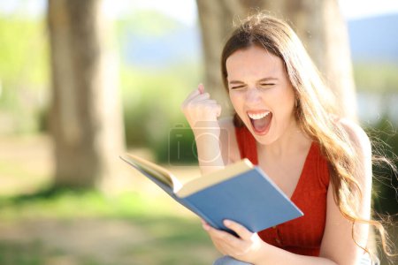 Mujer emocionada leyendo un libro de papel sentado en un parque