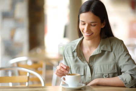 Foto de Mujer feliz sentada en una terraza del bar revolviendo taza de café - Imagen libre de derechos