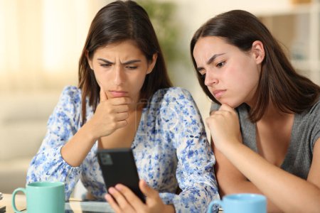 Confused friends watching media content on phone at home