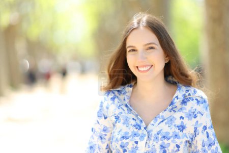 Front view portrait of a happy woman smiling at camera standing in a park a sunny day
