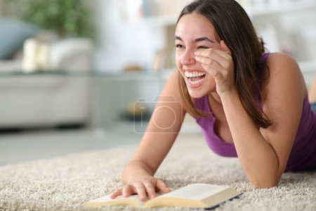 Fröhliche Frau lacht vergnügt und liest zu Hause ein auf dem Boden liegendes Lustbuch