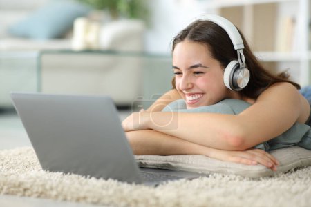 Mujer feliz viendo contenido de los medios de comunicación en el ordenador portátil acostado en una alfombra en casa
