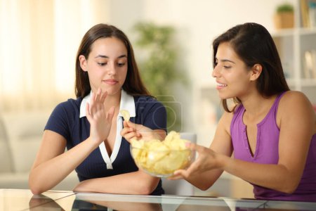 Foto de Mujer ofreciendo papas fritas a un amigo que la rechaza en casa - Imagen libre de derechos