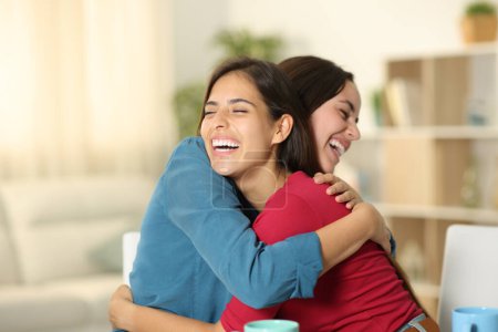 Two happy friends are hugging and laughing at home