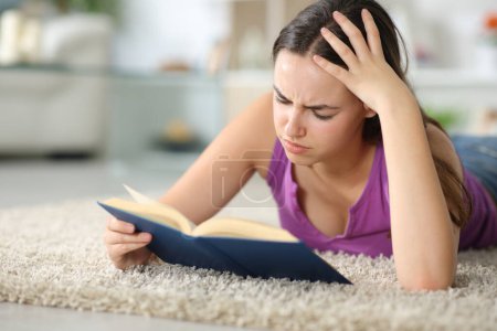 Mujer triste leyendo un libro de papel acostado en una alfombra en casa