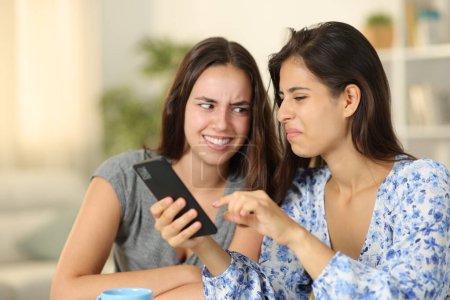 Two disgusted women watching nasty content on phone at home