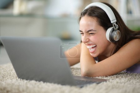 Happy woman watching media and laughing lying on the floor at home