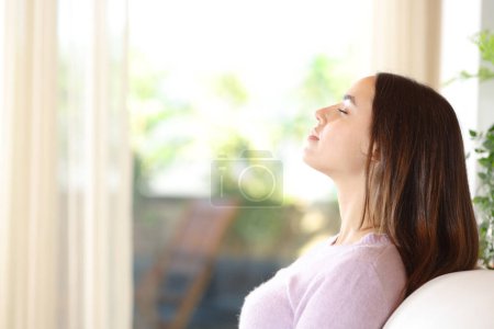 Side view portrait of a woman at home breathing fresh air sitting on a couch