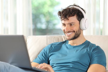 Hombre feliz viendo los medios de comunicación en el ordenador portátil sentado en un sofá en casa