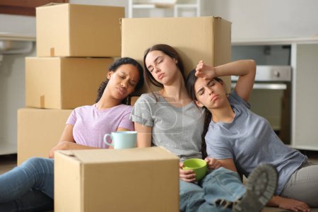 Three tired multi ethnic women moving house resting sitting on the floor