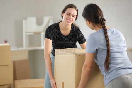 Two women suffering lifting heavy box moving home