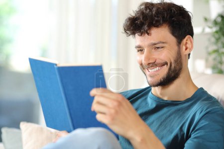 Happy man reading a paper book sitting on a couch at home