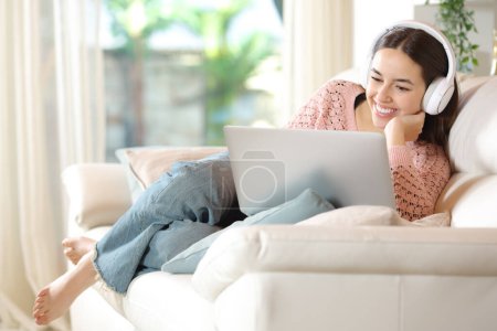 Ganzkörperporträt einer glücklichen Frau zu Hause, die die Medien am Laptop verfolgt