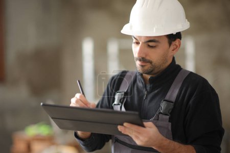 Foto de Trabajador de la construcción usando tableta digital para tomar notas trabajando en una casa - Imagen libre de derechos