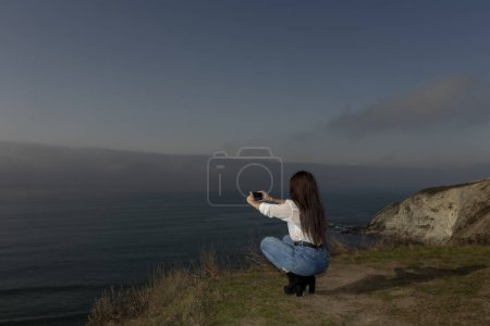 Téléchargez les photos : Jeune femme capture la beauté côtière grâce à son objectif mobile - en image libre de droit