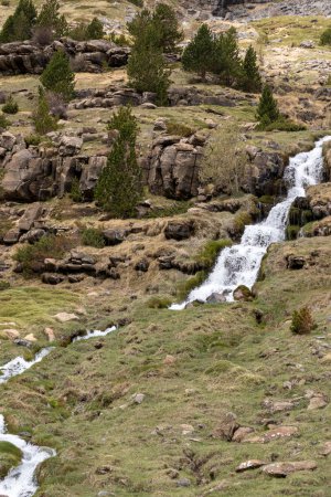 serene landscape with a cascading waterfall, rocky terrain, sparse green vegetation, and a cloudy sky