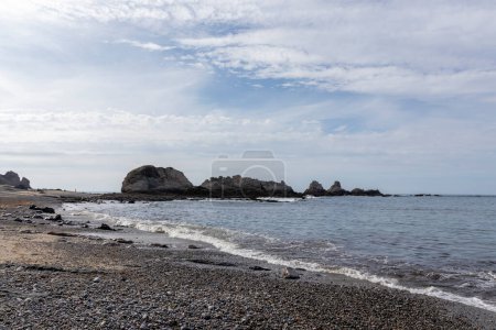 peaceful pebble beach with calm waters, large rocks, and a cloudy sky, creating a tranquil atmosphere