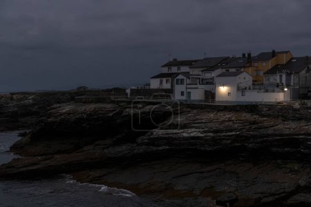 town at dusk, houses on rocky shores, dark clouds overhead, waves gently crashing, a serene yet somber atmosphere