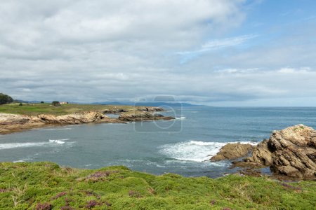 scenic coastal landscape with rocky shores, greenery, and a cloudy sky overlooking the calm blue ocean.