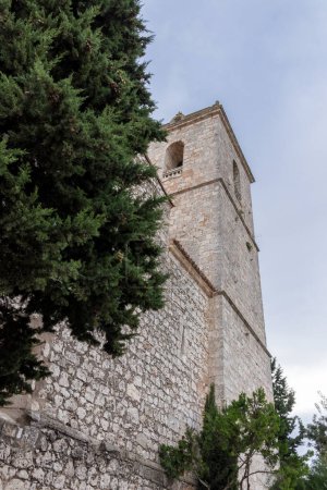 Téléchargez les photos : Une vieille tour de pierre, probablement partie d'une église ou d'un château, debout à côté d'un arbre vert luxuriant sous un ciel nuageux - en image libre de droit