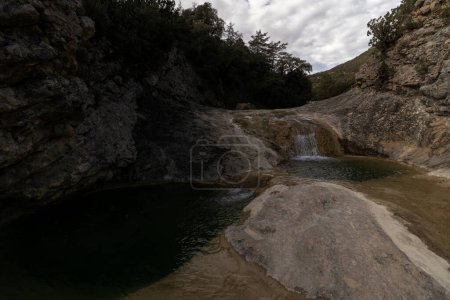 cascade isolée se jette dans un étang serein, entouré de terrains rocheux et de verdure luxuriante, évoquant un sentiment de tranquillité