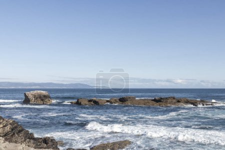 serene seascape with rocky formations, waves crashing under a clear blue sky, evoking a sense of calm and natural beauty.