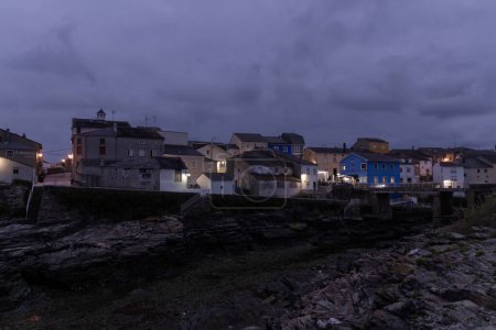 tranquil coastal town under the enigmatic embrace of dusk, where artificial lights and natural darkness create a scene of quiet beauty and mystery