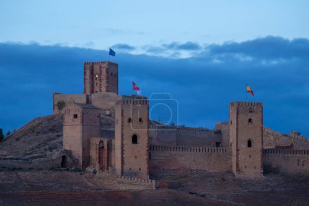 mittelalterliche Burg mit Türmen, die verschiedene Fahnen schwenken, steht majestätisch vor einem wolkenverhangenen Abendhimmel