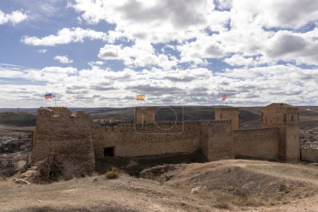 historic stone fortress with three flags on top overlooks a vast landscape under a cloudy sky, showcasing architectural and natural beauty