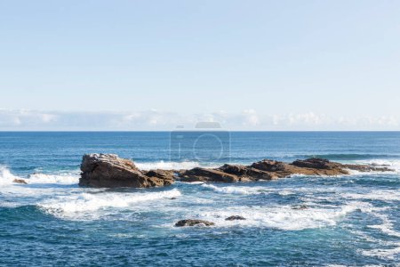 serene seascape with rocky formations amidst gentle waves, under a clear sky, exuding calmness and natural beauty
