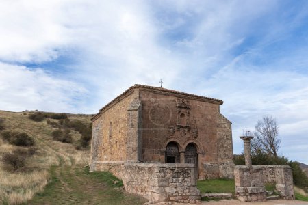 viejo edificio de piedra con una cruz, posiblemente una iglesia, en medio de un paisaje natural bajo un cielo parcialmente nublado.