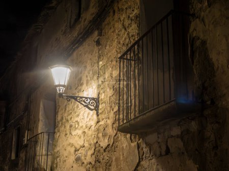 lit streetlamp illuminates an aged wall and balcony at night, creating a moody, atmospheric, and historical scene