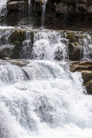 lebhafter Wasserfall, der sich über Felsen ergießt, von Moos umgeben und die Energie und Schönheit der Natur verkörpert