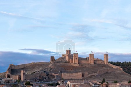 Photo for Ancient stone castle with multiple towers overlooks a small town, set against a backdrop of a cloudy sky - Royalty Free Image