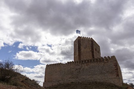 ancienne forteresse en pierre surplombant une ville moderne contre les collines et un ciel nuageux