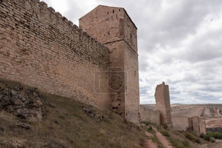 alte, hohe Steinmauer und Turm, Teil einer Festung, unter wolkenverhangenem Himmel mit karger Umgebung.