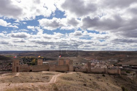 ancienne forteresse en pierre surplombant une ville moderne contre les collines et un ciel nuageux