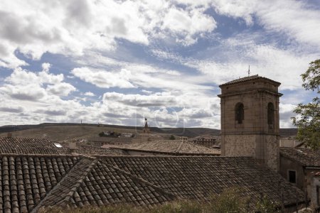 historic town with tiled roofs, a bell tower, and fluffy clouds over rolling hills