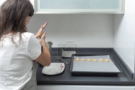 Photo for Individual in a kitchen, preparing cookies on a baking sheet, with modern aesthetics and privacy - Royalty Free Image